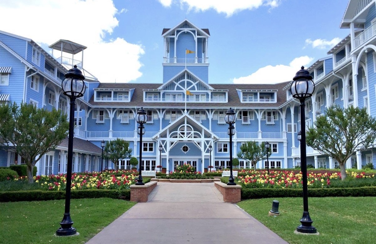 Fachada azul pastel y blanca de Disney's Beach Club Resort con jardines y faroles