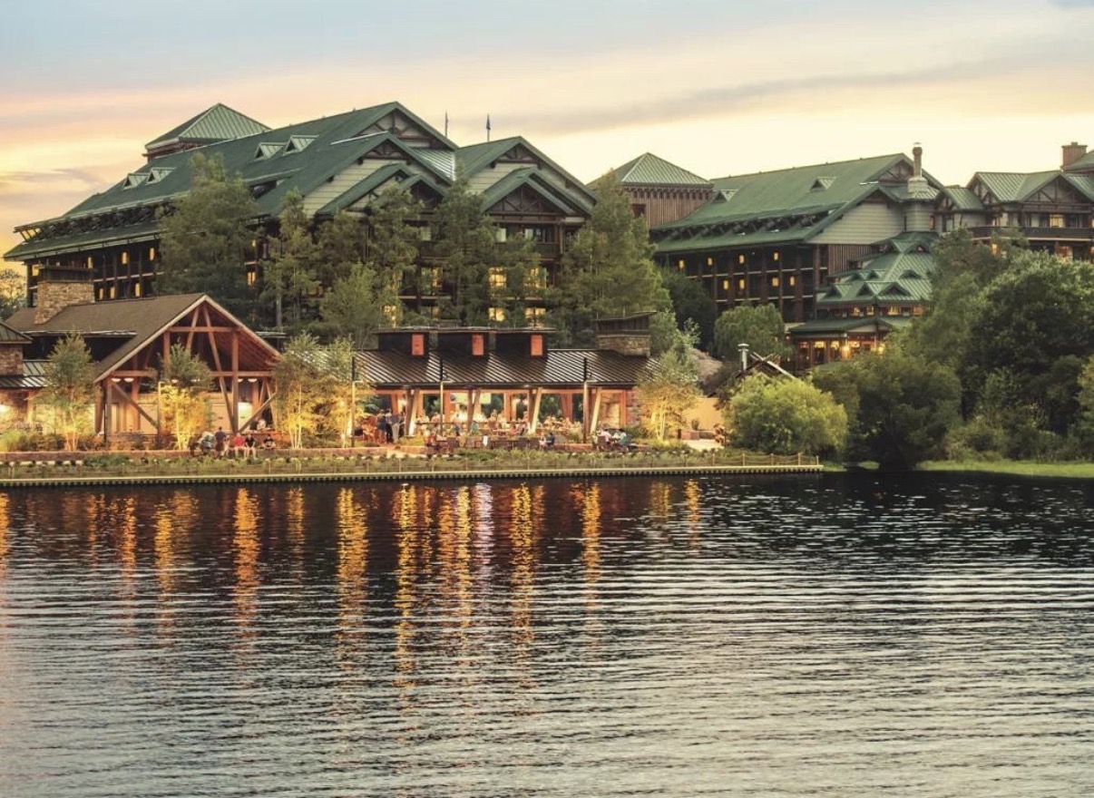 Exterior de Disney's Wilderness Lodge al atardecer visto desde Bay Lake, con techos verdes y bosque